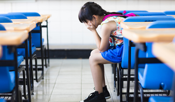 distraught middle-school child with head in hands, sitting in an empty class room