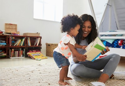 Mother And Baby Daughter Reading Book In Playroom Together