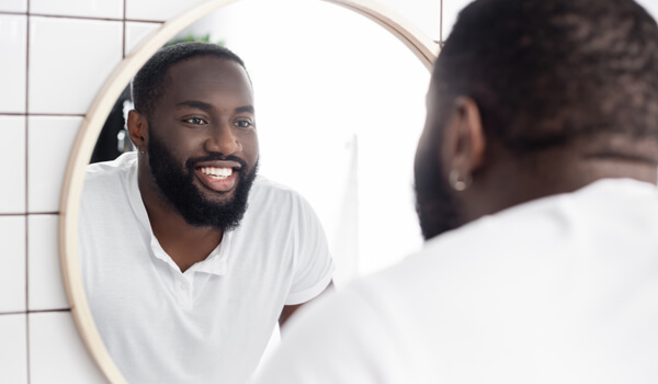 Bearded man smiles in the bathroom mirror.