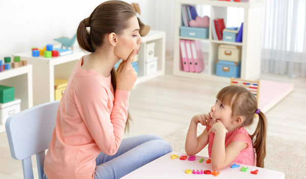 A teacher and young child practice vowel sounds in a classroom.