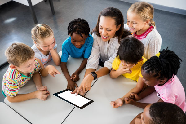 A teacher points at a tablet while students look on