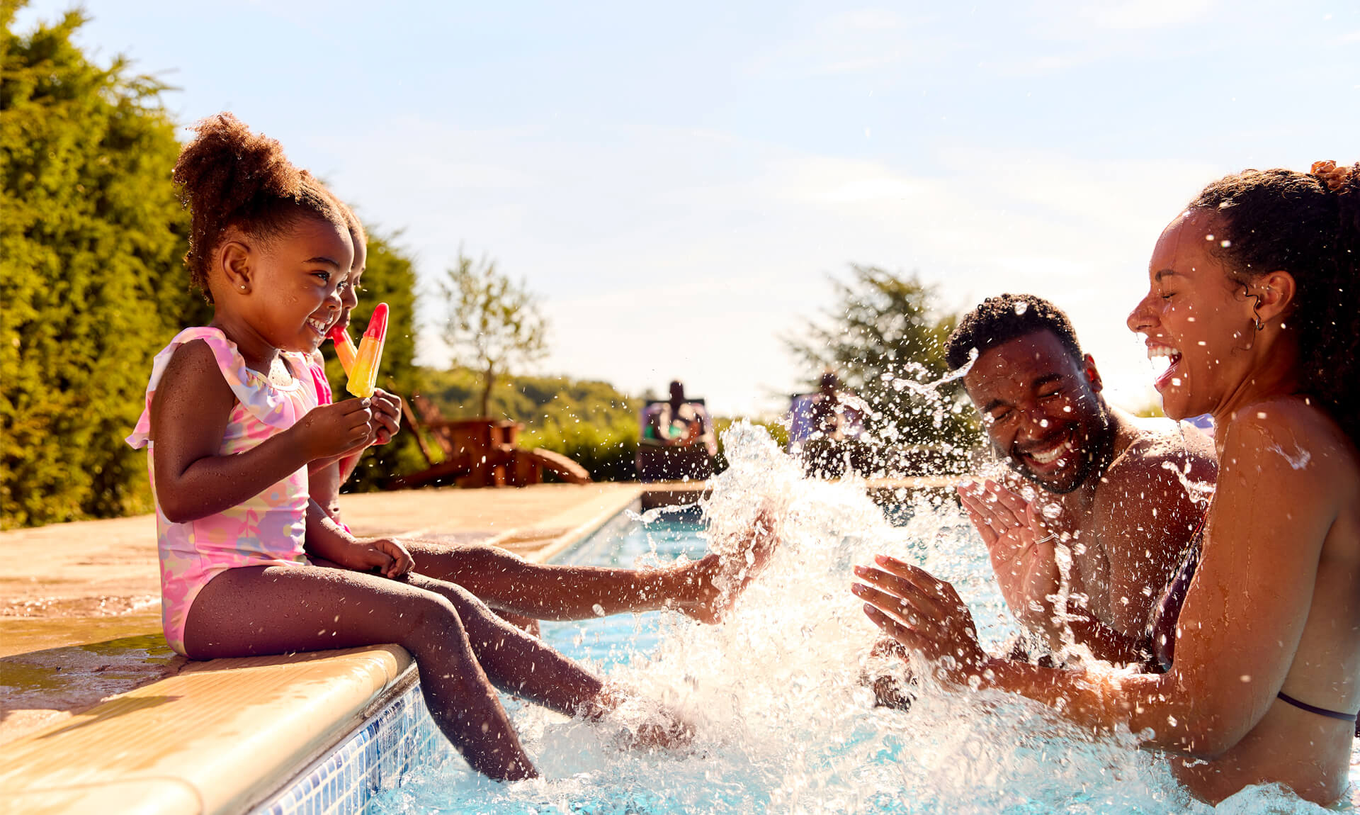 family splashes in sunny pool while children eat popsicles