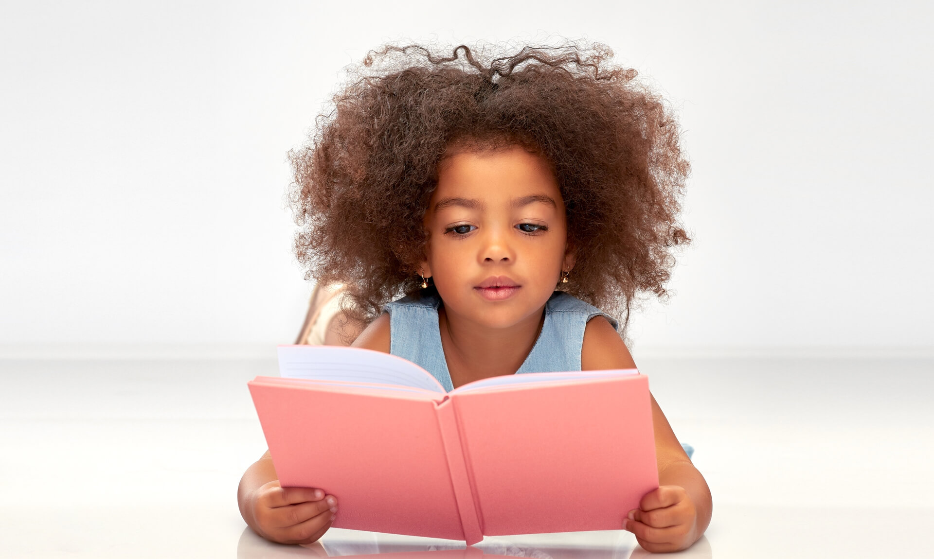 young girl intently reads a pink book