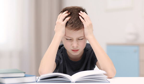 young boy with a book in front of him holds his head in his hands and has his eyes closed in frustration young boy with a book in front of him holds his head in his hands and has his eyes closed in frustration