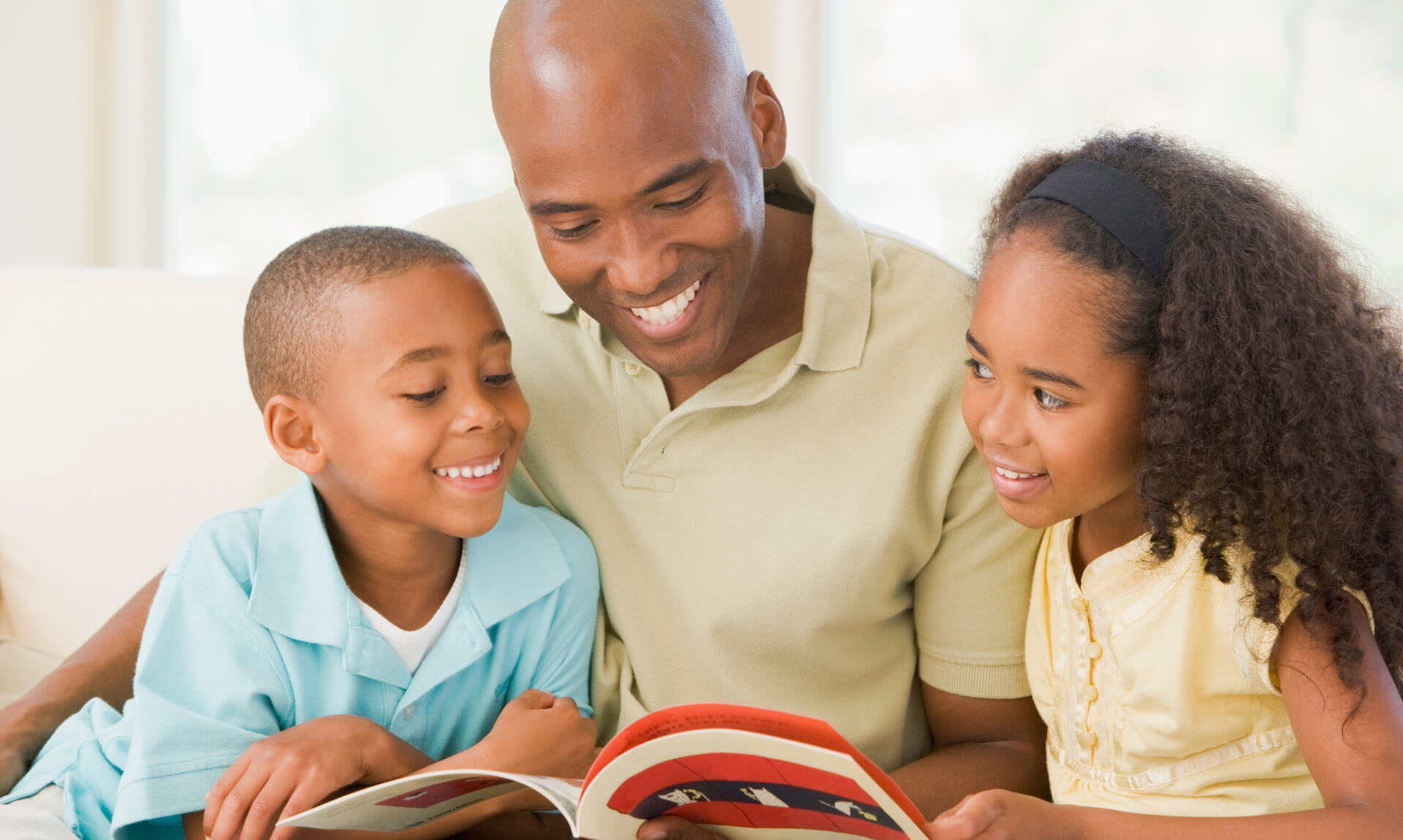 Man and two children sitting in living room reading book and smiling.