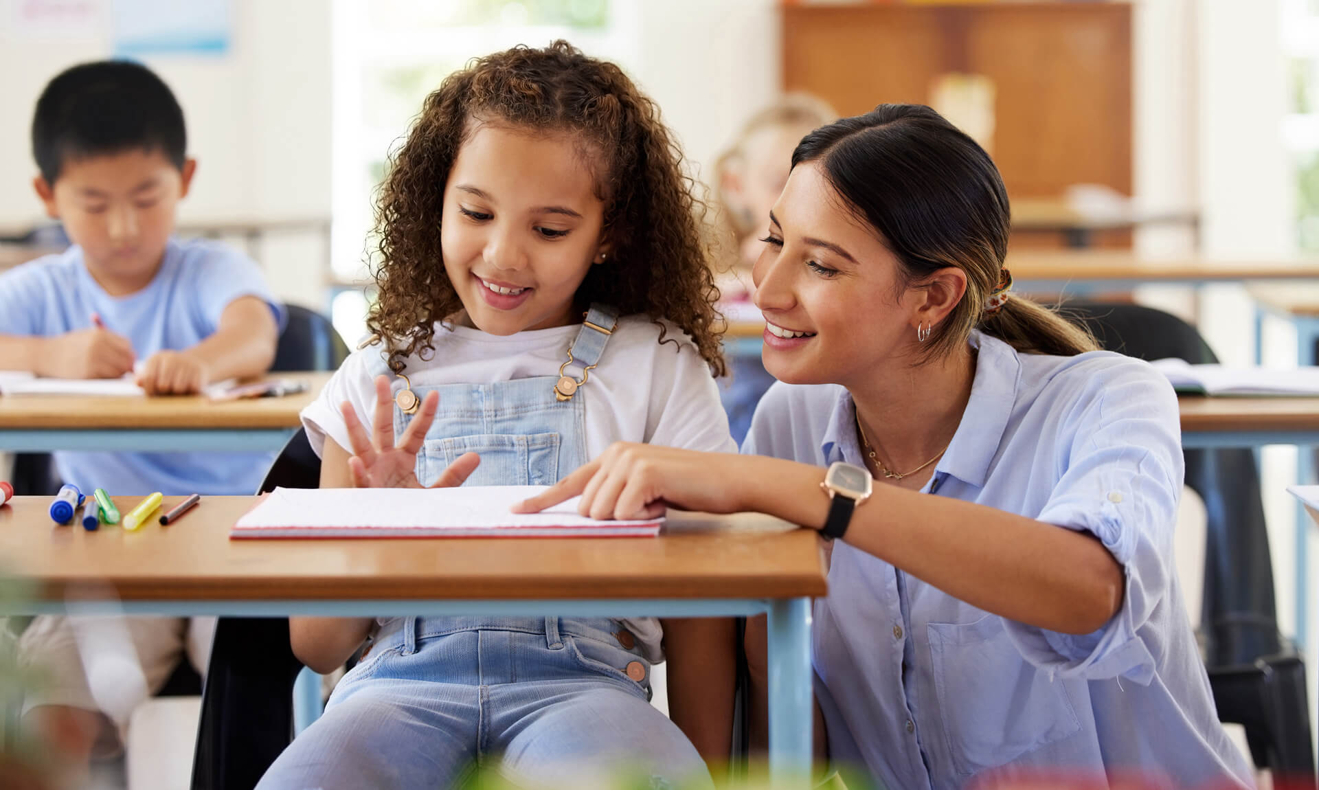 Teacher helping girl in classroom with her work.