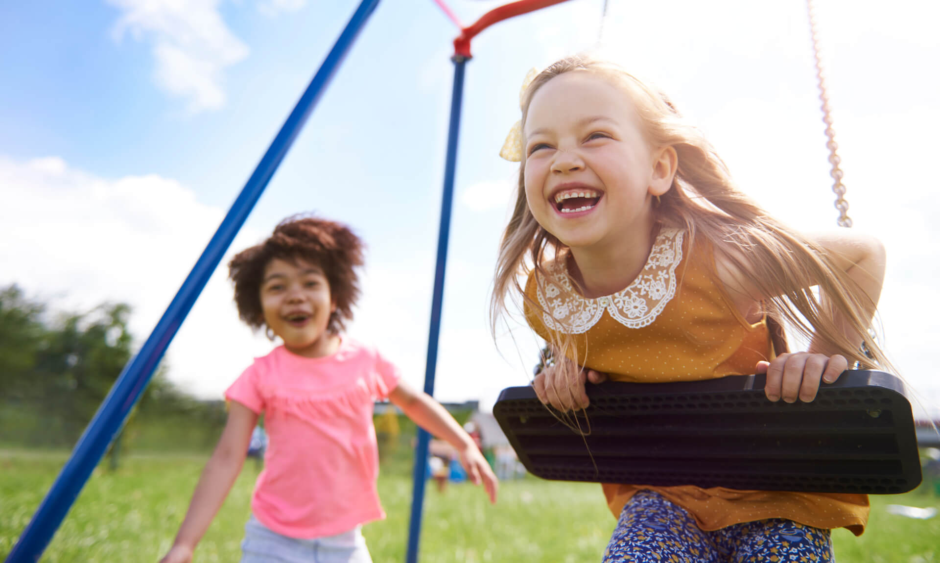 Developmental Milestones Best friends playing together on a swingset in the park.