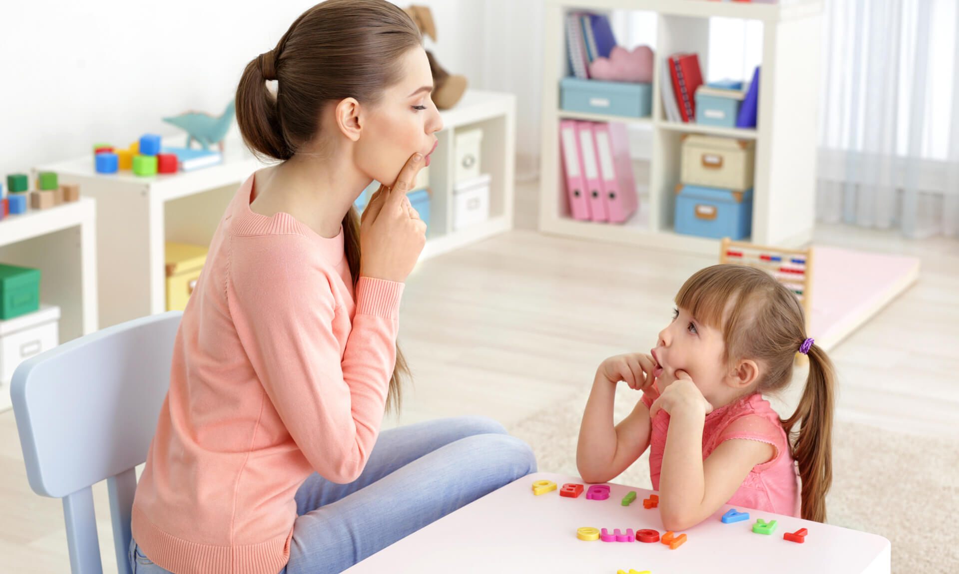 Later Language Development A teacher and young child practice vowel sounds in a classroom.