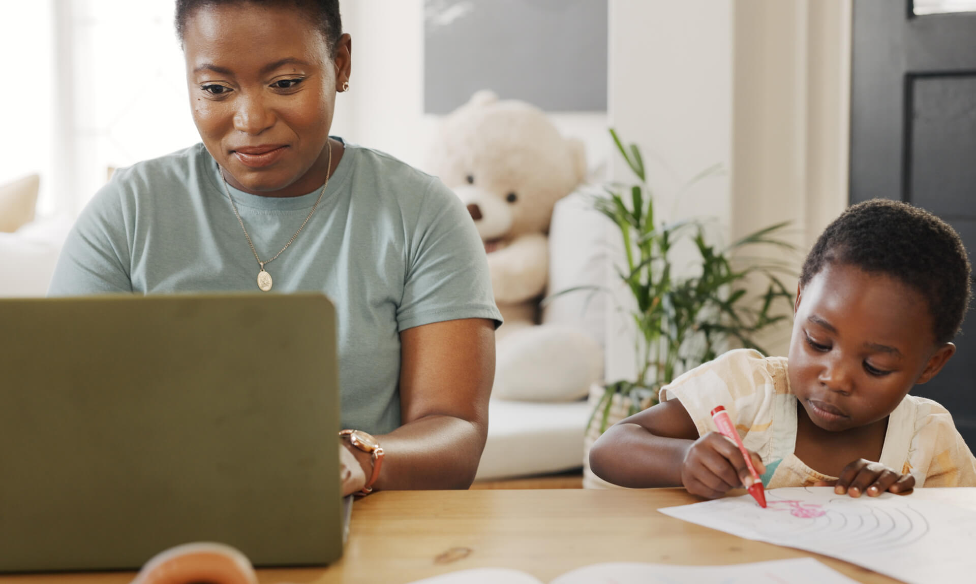 Mother typing on laptop while daughter colors nearby.