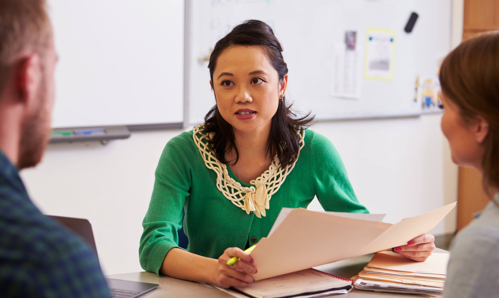 Teacher at desk talking to parents.