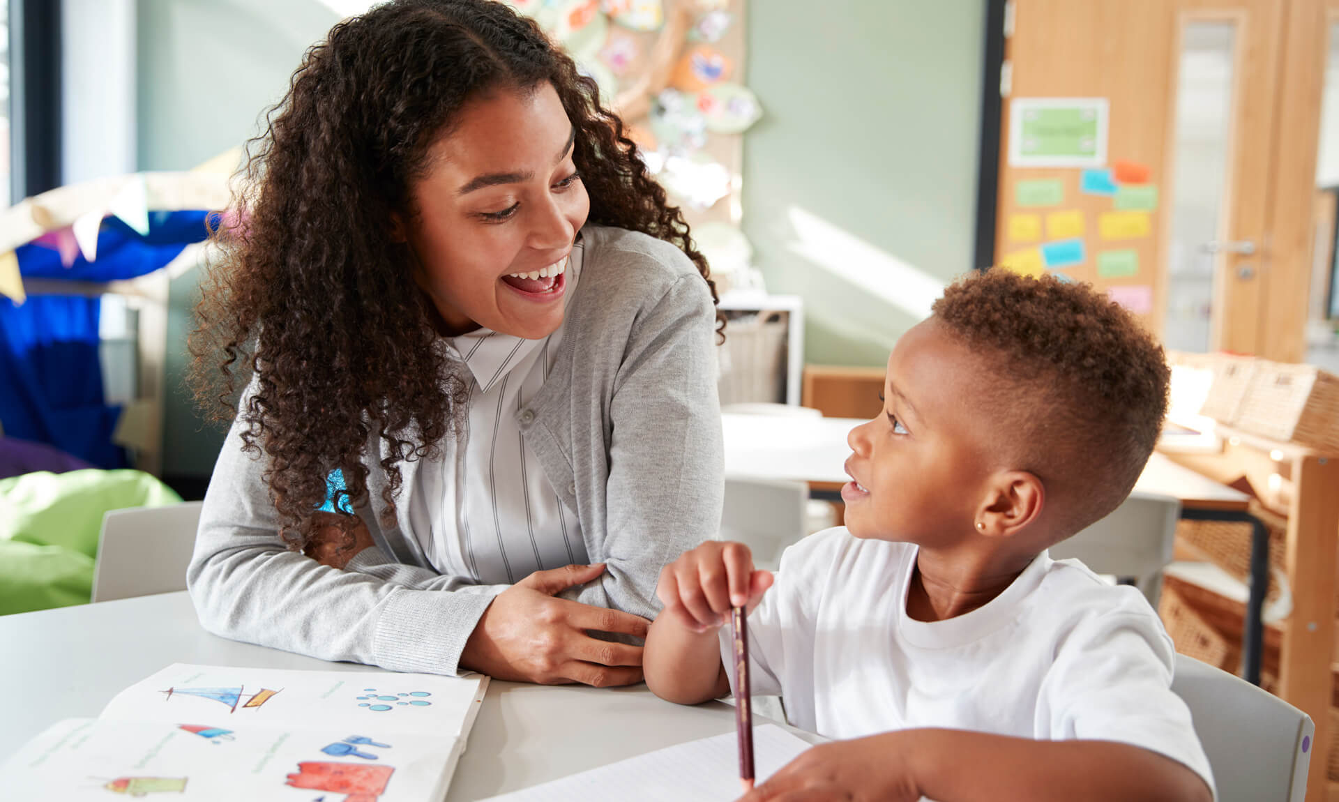 Screening Female school teacher working one on one with a young student, sitting at a table smiling at each other, close up.