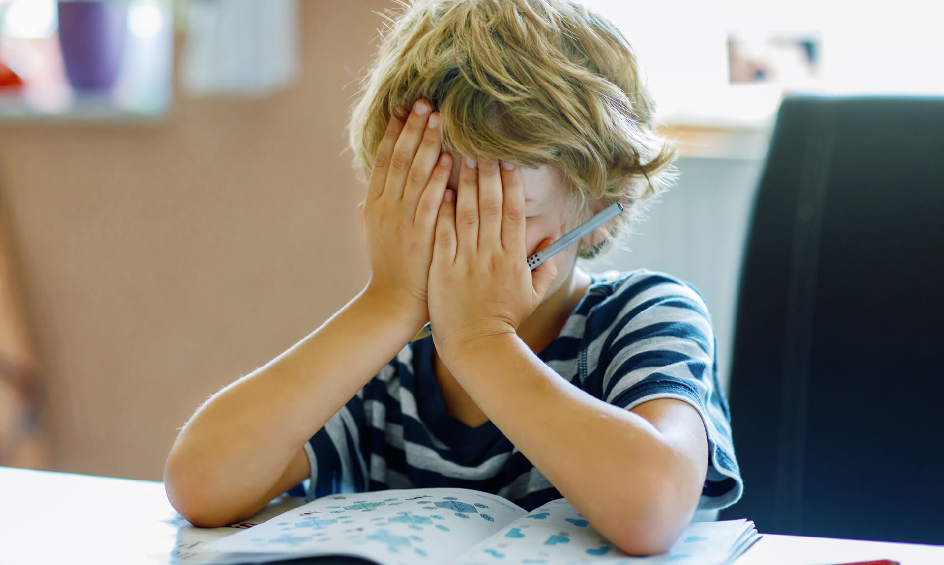 Portrait of tired upset boy doing homework in kitchen at home.