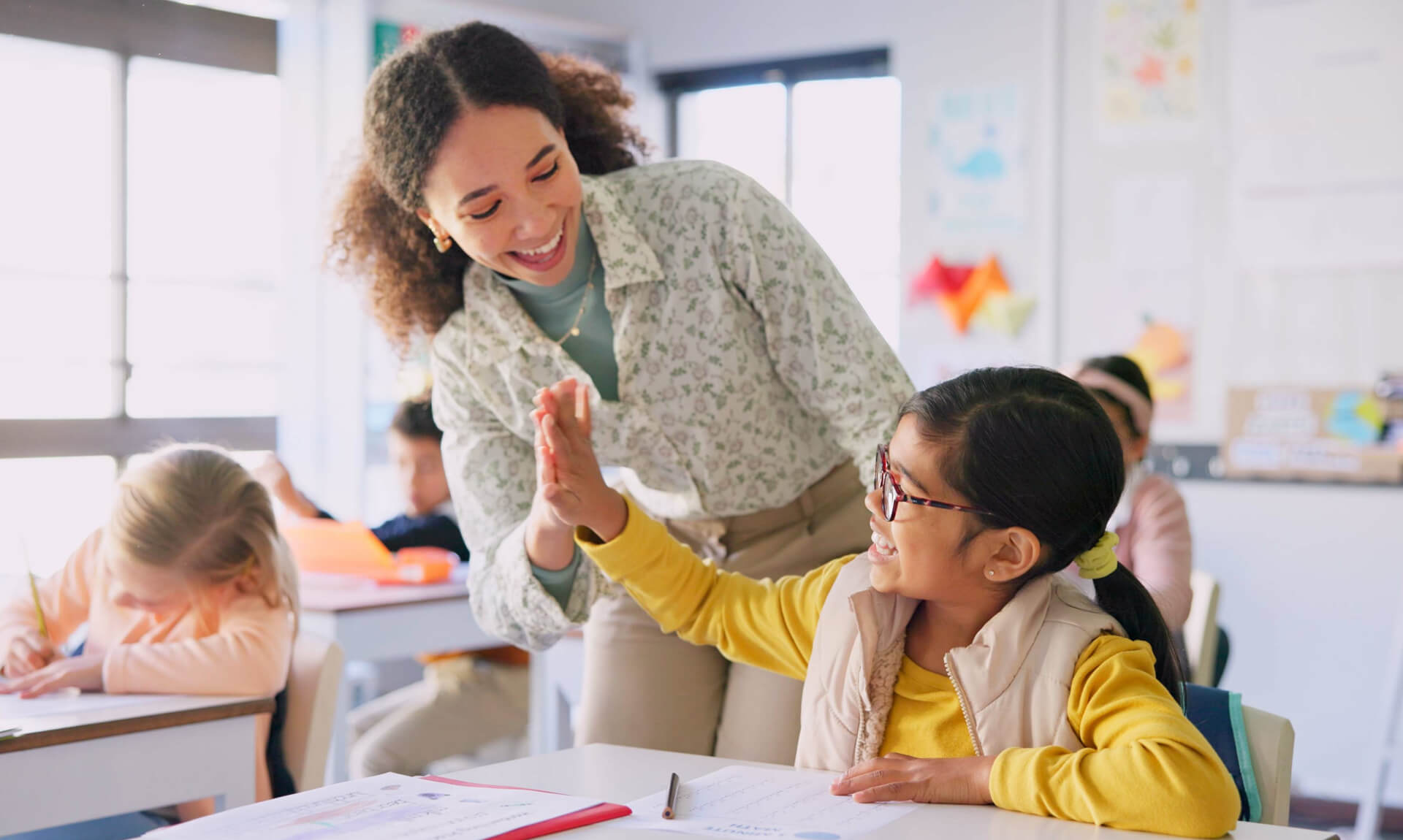 Teacher high fives girl in classroom.