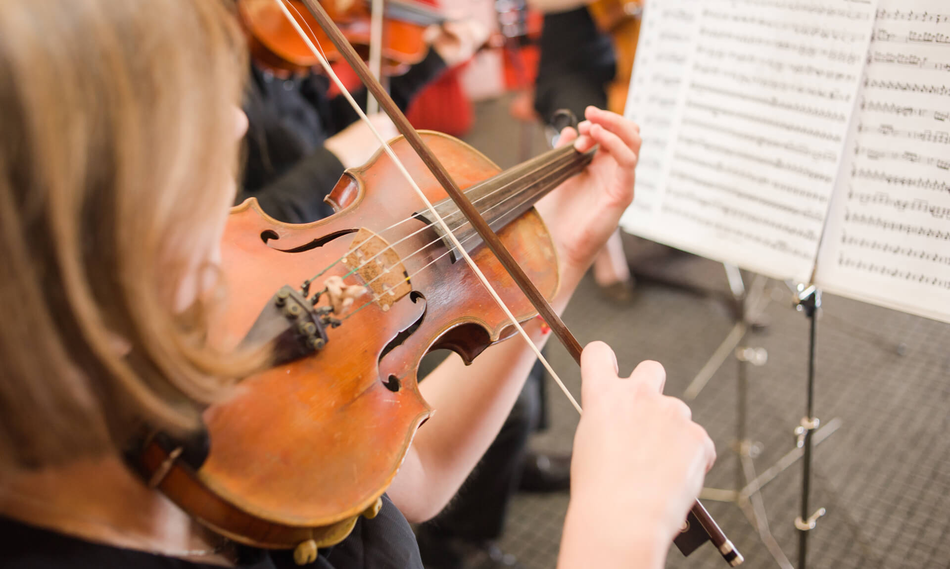 Closeup of girl in orchestra playing a violin to sheet music.