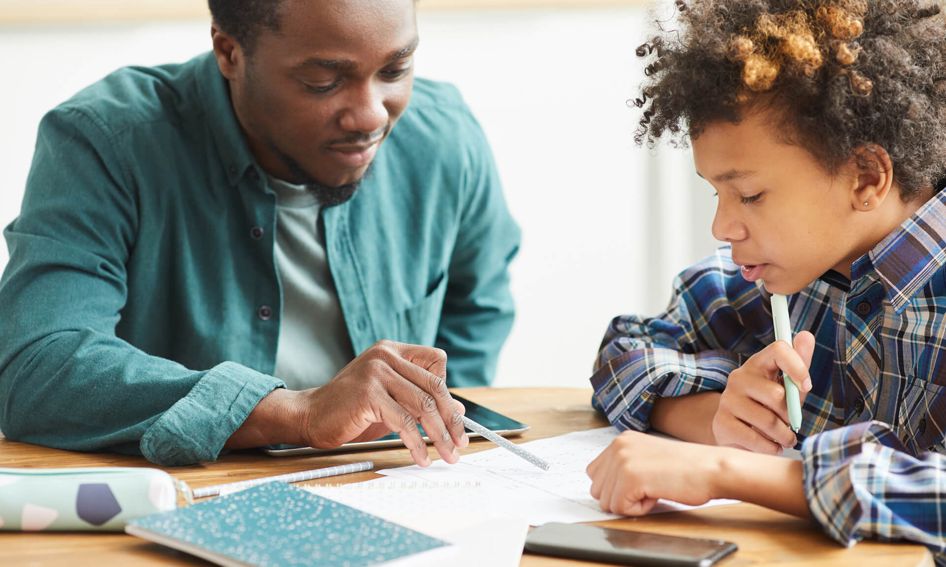 Teacher sitting at the table together with a student and explaining the lesson to him.