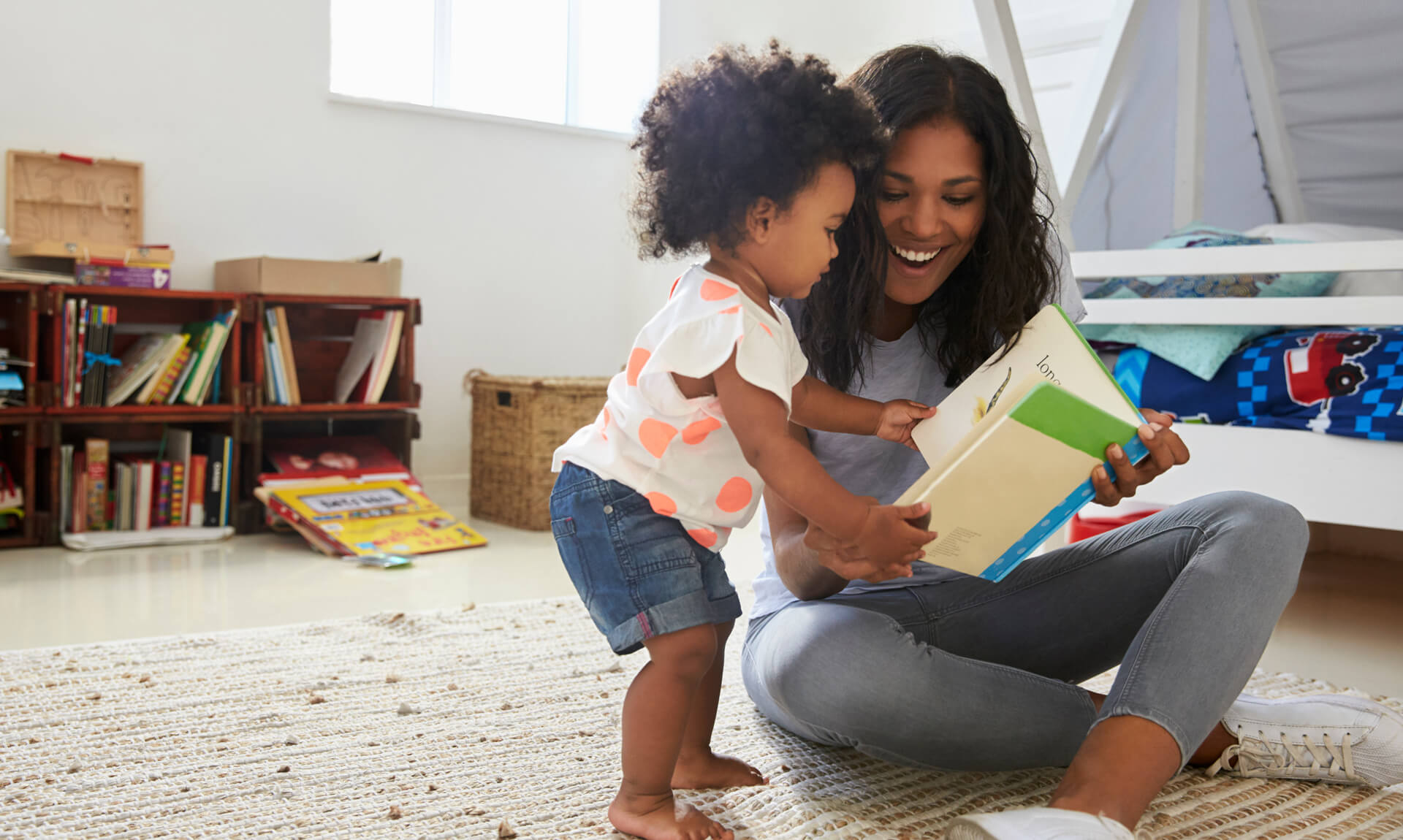 Mother And Baby Daughter Reading Book In Playroom Together