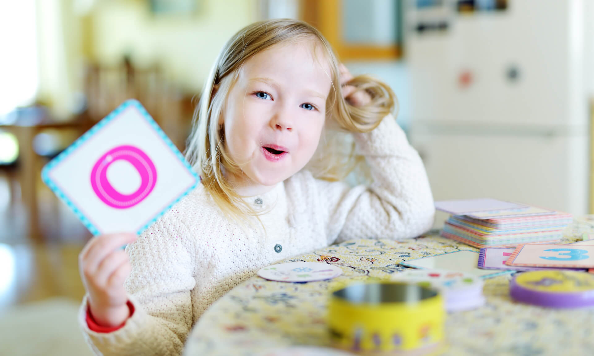 young girl presents alphabet flash card while sitting at a table
