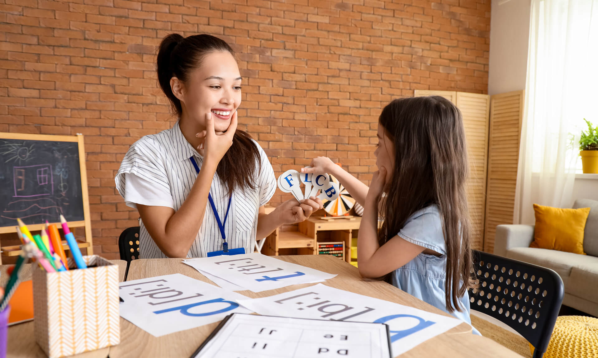 speech therapist teaching little girl how to pronounce letters in office