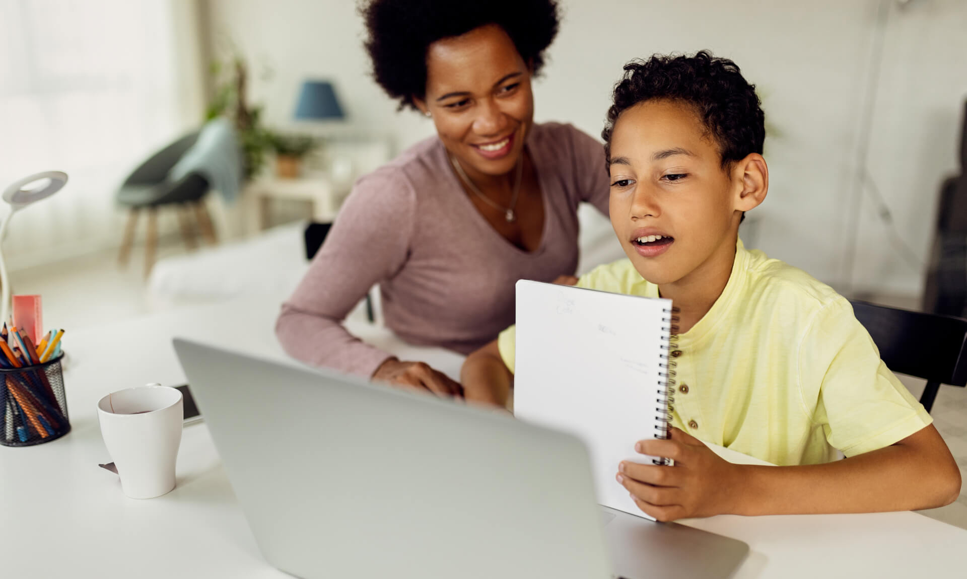 Child working on school assignment on computer while his mom looks on.