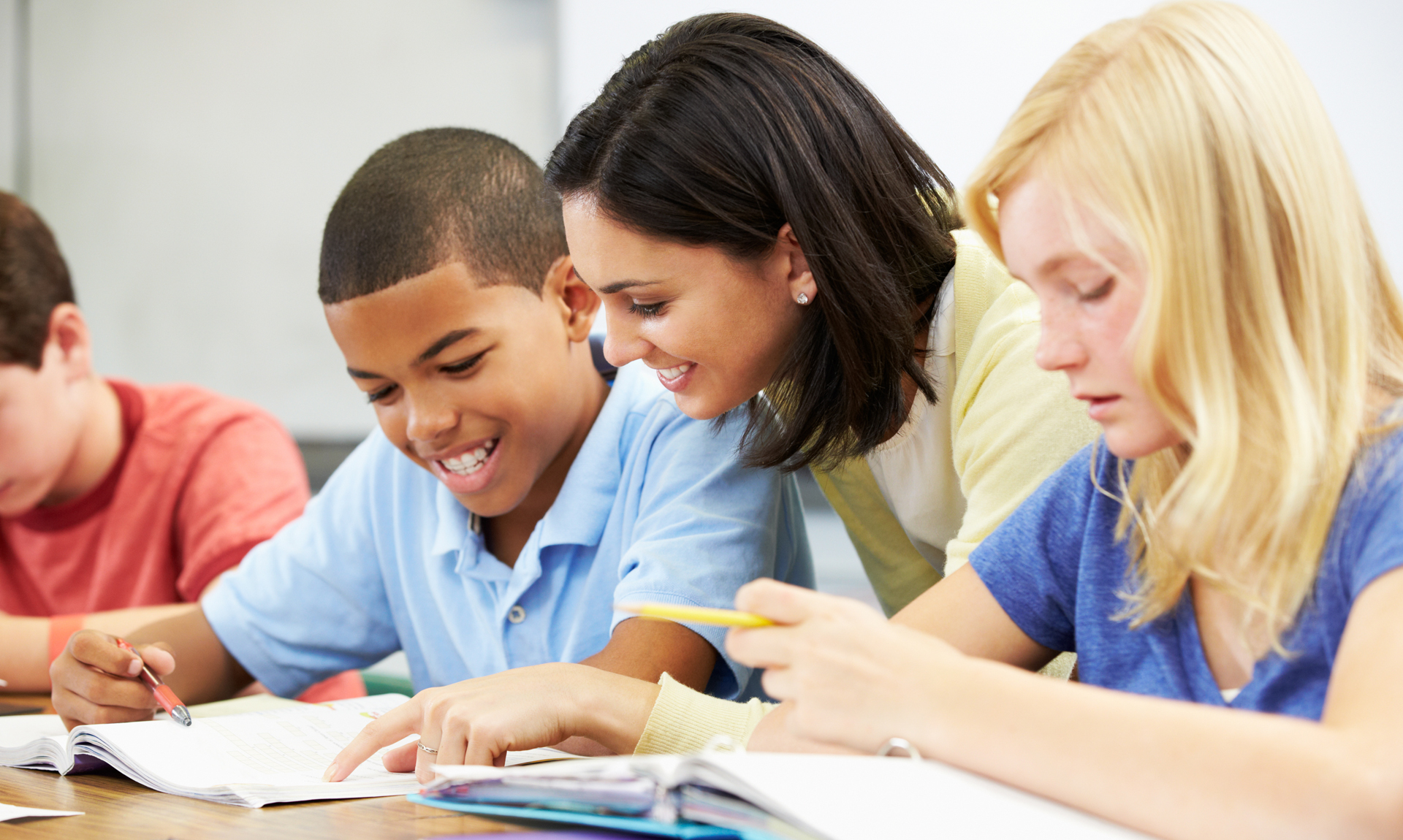 Teacher Helping Pupils Studying At Desks In Classroom