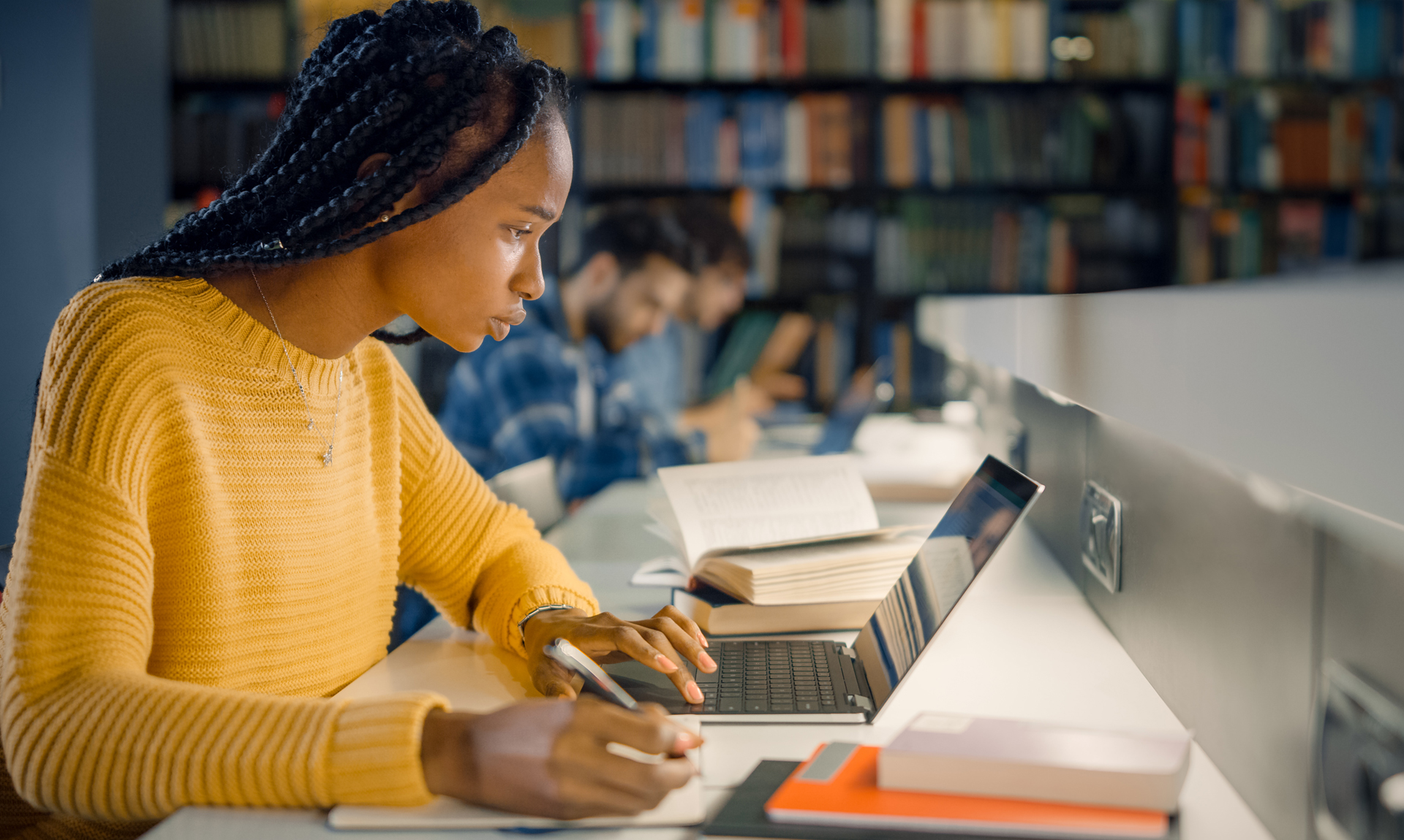 woman looks at laptop while taking notes in library
