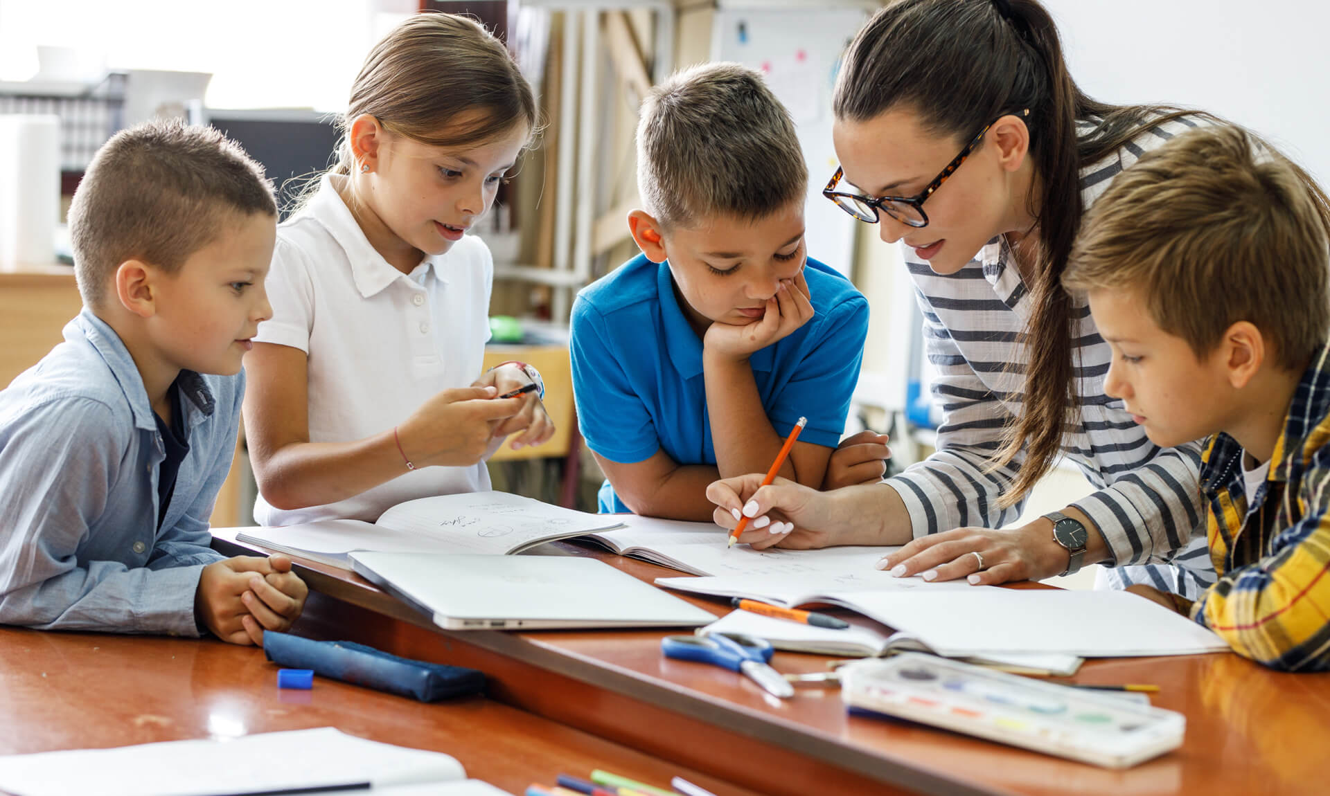 teacher explains workbook in classroom while young students look on