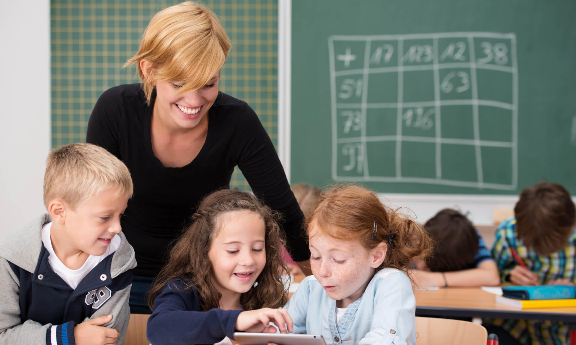 teacher watches three students enjoying lesson on tablet