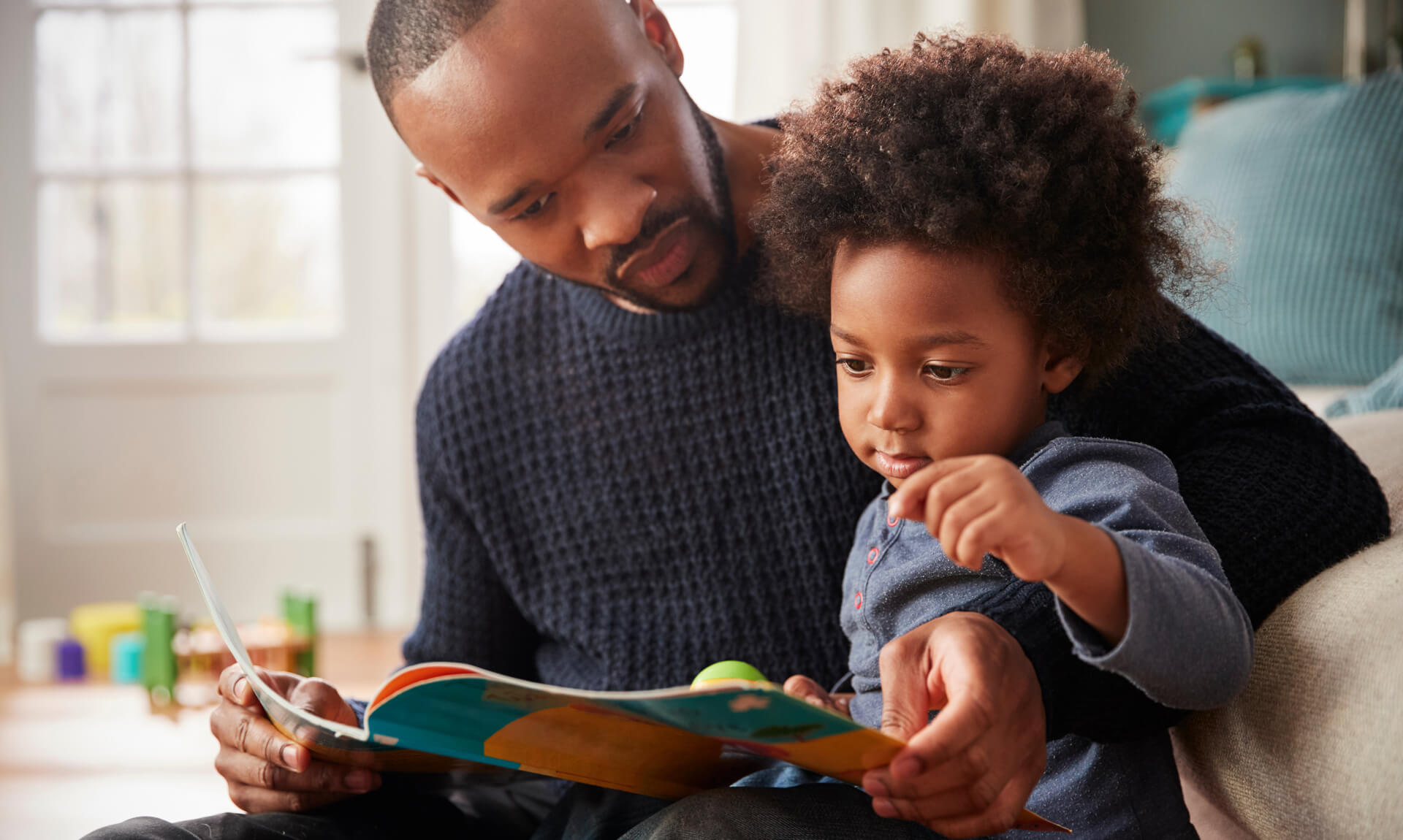 Fater and young son read a book on the couch together.