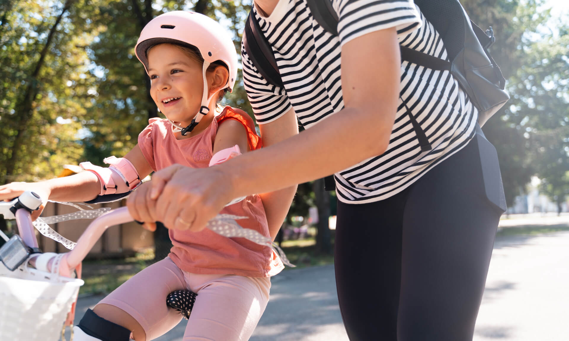 mother helps daughter ride a bicycle in a park