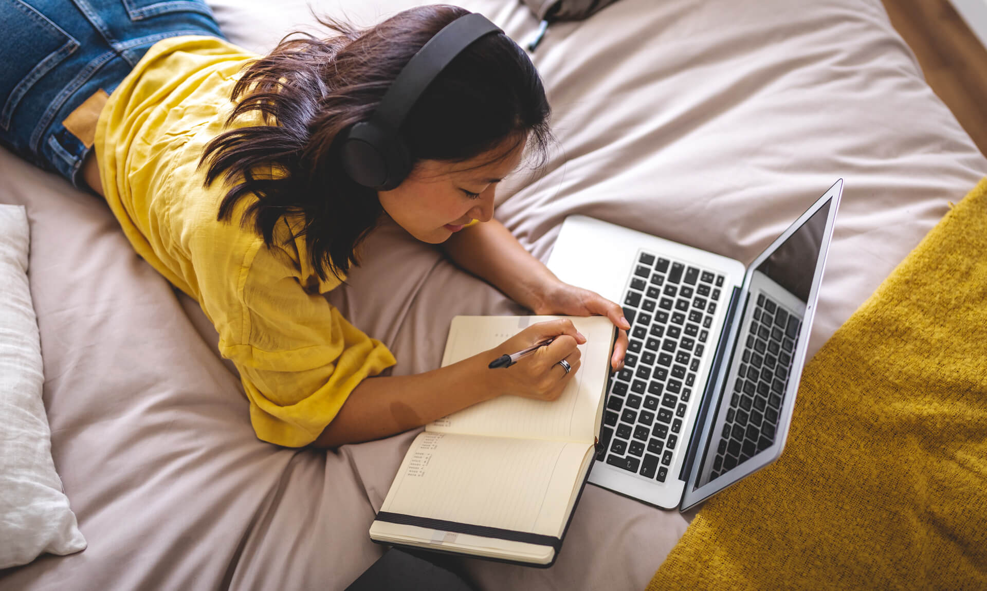 girl studies on bed using laptop and notebook