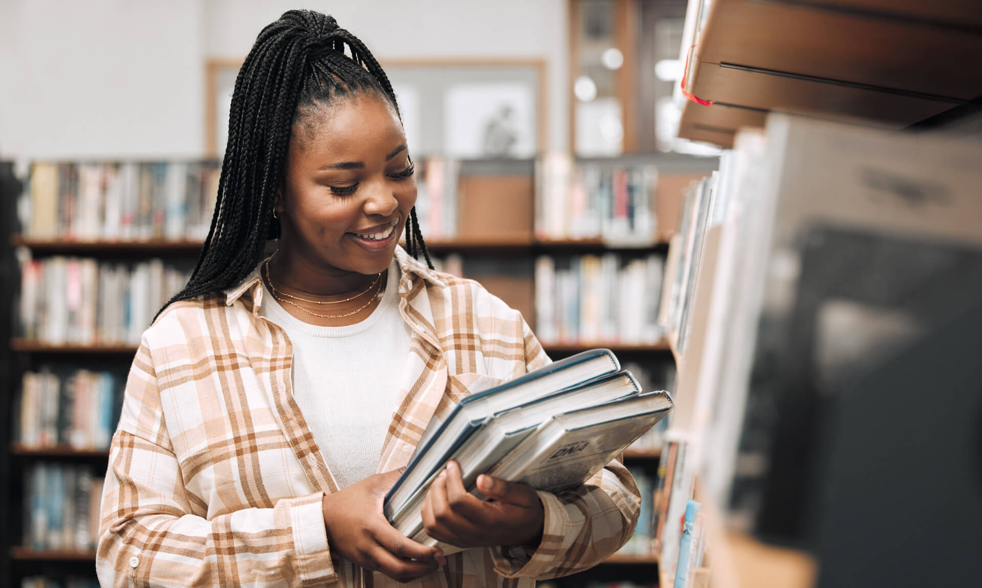 Young college student smiling while standing between bookshelves in a university library.